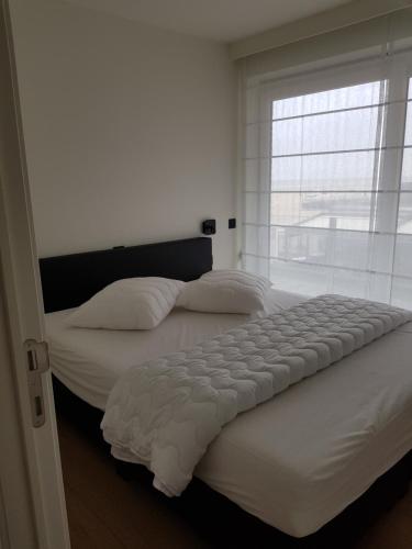 1 dormitorio blanco con 2 camas y ventana en Koksijde Zeedijk La Digue 101 appartement - frontaal zeezicht - adult only, en Koksijde