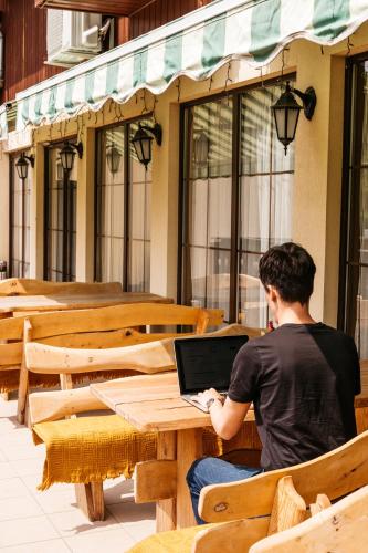 a man sitting at a bench with a laptop at Hotel Chata Za Wsią in Mysłakowice