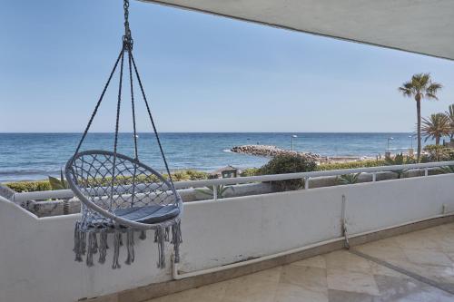 una silla mecedora en un balcón con vistas a la playa en Seafront Apartment with 2 bedrooms in Puerto Banús, en Marbella