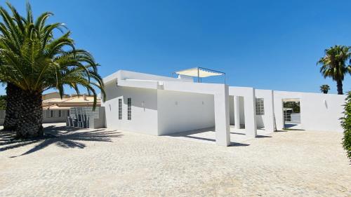 a white building with a palm tree in front of it at Moderna - Private Pool - 8 Guests - Quarteira in Quarteira
