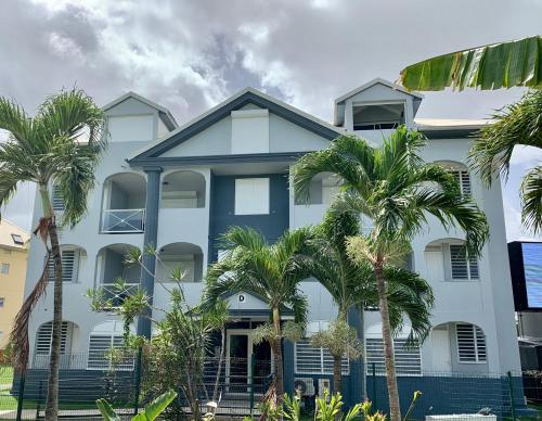 un edificio blanco con palmeras delante en Karaibes Residence, en Le Gosier