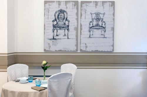 a table with white chairs and two drawings of chairs at Hotel Olimpia in Forte dei Marmi