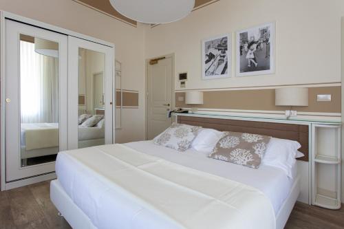 a white bedroom with a large bed and a mirror at Hotel Olimpia in Forte dei Marmi