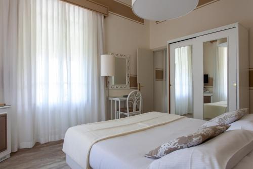 a white bedroom with a large white bed with a mirror at Hotel Olimpia in Forte dei Marmi