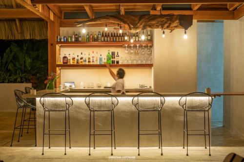 a woman standing at a bar with three bar stools at Hotel Gringo Perdido in El Remate