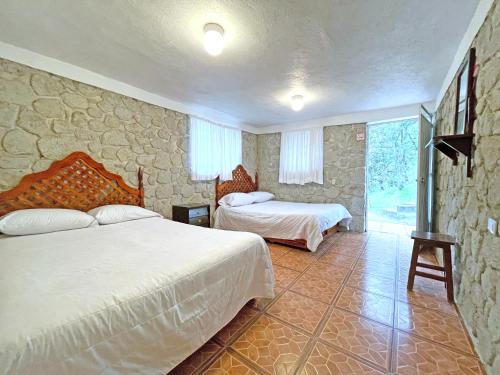 1 dormitorio con 2 camas y pared de piedra en Hotel Chinguirito, en Villa del Carbón