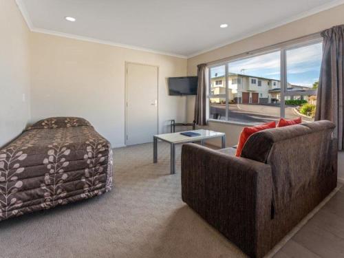 a bedroom with a couch and a bed and a window at Cottage Park Thermal Motel in Tauranga