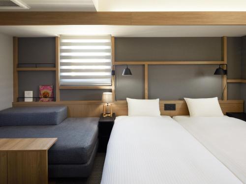 two beds and a couch in a room at LAMP LIGHT BOOKS HOTEL sapporo in Sapporo