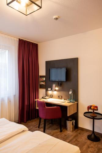 a hotel room with a desk with a red chair at Arcus Hotel München Messe in Feldkirchen