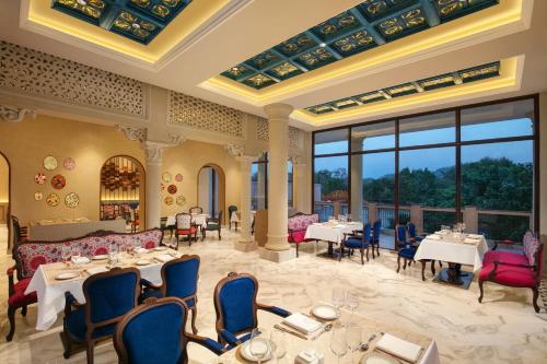 Un restaurante con mesas y sillas y grandes ventanales. en Pilibhit House, Haridwar – IHCL SeleQtions, en Haridwar