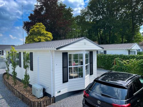 a white tiny house with a car parked in front at Chalet Natuurrijk in Oisterwijk