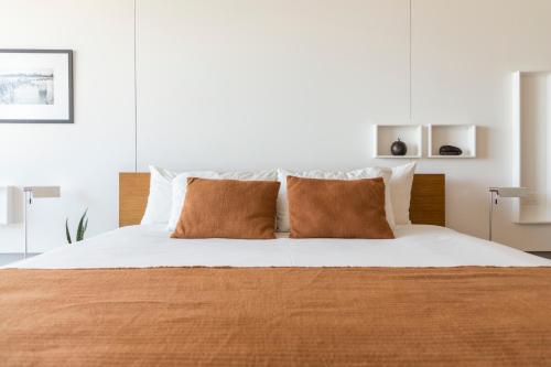 1 dormitorio con 1 cama con sábanas blancas y almohadas marrones en Opta Coliving Punta Carretas, en Montevideo