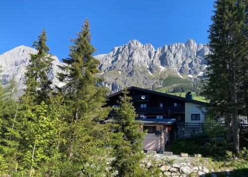 a building with mountains in the background with trees at Appartementhaus Hochkönig - Panoramablick in Mühlbach am Hochkönig