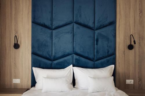 a bed with a blue headboard with white pillows at Nedei Hotel&Spa Transalpina in Martinie