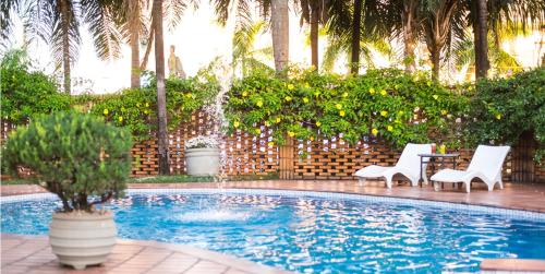 uma piscina com duas cadeiras, uma mesa e uma fonte em Vila Romana Park Hotel em Três Lagoas
