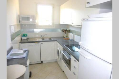 une cuisine avec des armoires blanches et un réfrigérateur blanc dans l'établissement F2 Climatisé Piscine Proche Plage, à Cavalaire-sur-Mer