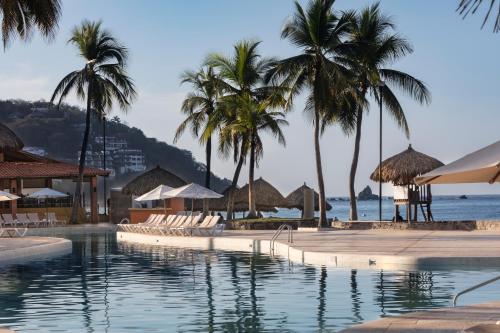 uma piscina com cadeiras e palmeiras e o oceano em Holiday Inn Resort Ixtapa All-Inclusive, an IHG Hotel em Ixtapa