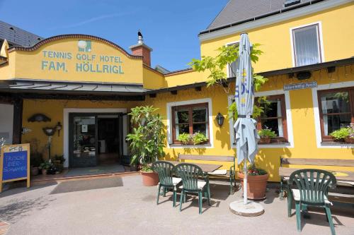 a yellow building with chairs and an umbrella at Tennis Golf Hotel Höllrigl in Kottingbrunn