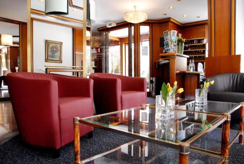 a living room with red chairs and a glass table at Ambassador Parkhotel in Munich