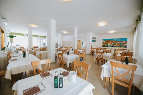 um restaurante com mesas brancas e cadeiras de madeira em Hotel Gloria em Lignano Sabbiadoro