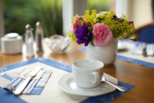 a table with a cup of coffee and a vase of flowers at Hotel an der Schlei Garni in Fahrdorf