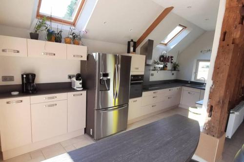 une cuisine avec un réfrigérateur en acier inoxydable et des armoires blanches dans l'établissement Maison en colombage rénovée, à La Fontenelle