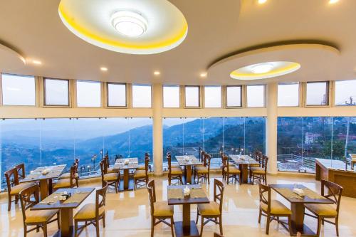 a restaurant with tables and chairs and large windows at Himalaya Drishya Resort in Dhulikhel