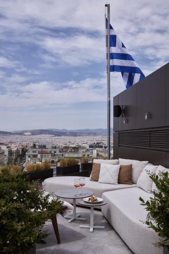 a white couch and a table on a balcony with a flag at Athens Capital Center Hotel - MGallery Collection in Athens