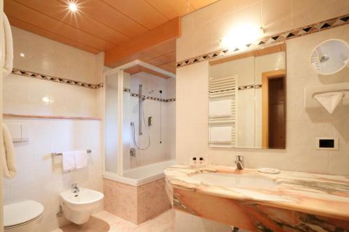ein Bad mit einem Waschbecken, einer Dusche und einem WC in der Unterkunft Hotel Condor in Wolkenstein in Gröden