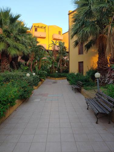 a courtyard with two benches and a building with palm trees at Sa Marinedda Guest Apartment - self check-in - IUN R1644 in Olbia