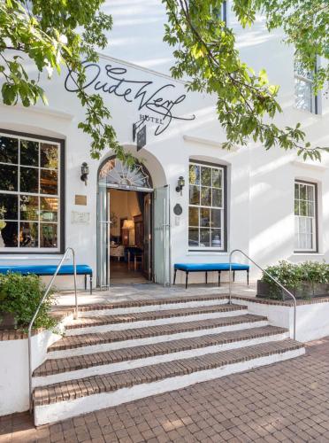 a white building with blue benches in front of it at Oude Werf Hotel in Stellenbosch