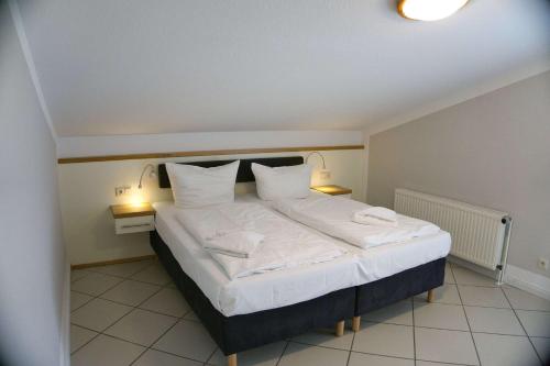 1 dormitorio con 1 cama grande con sábanas y almohadas blancas en FeWo mit Meerblick, gratis Nutzung vom AHOI Erlebnisbad und Sauna in Sellin - Haus Blick zur See FeWo 10, en Göhren