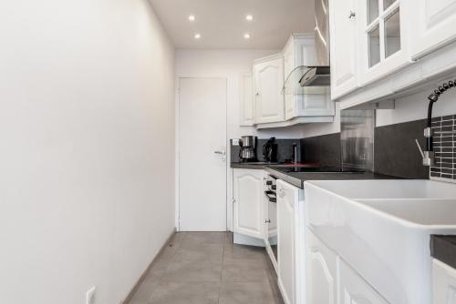 una cocina blanca con armarios blancos y fregadero en Appartement en front de mer avec terrasse et vue mer en Arromanches-les-Bains