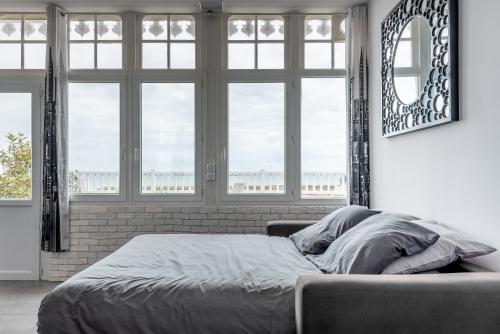 a bed in a room with windows and a bed sidx sidx sidx at Appartement en front de mer avec terrasse et vue mer in Arromanches-les-Bains