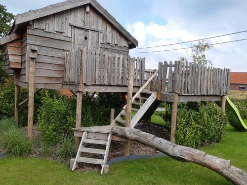 a wooden tree house with a ladder and a slide at vakantiehuis zoetendaal in Reningelst