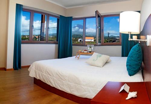 a bedroom with a large bed with blue curtains and windows at Baia da Barca in Madalena