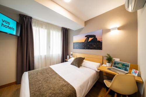 Habitación de hotel con cama y escritorio con ordenador portátil en Hotel Vas Vitoria AutoCheckIn, en Vitoria-Gasteiz