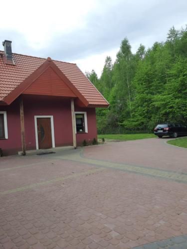 a red house with a driveway in front of it at Domek letniskowy w lesie 6 -7 osób in Wydminy