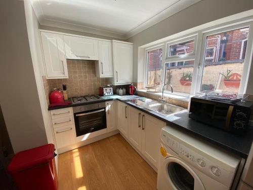 a kitchen with white cabinets and a sink and a dishwasher at Sandown Seaside Apartment Ground Floor 4 in Sandown
