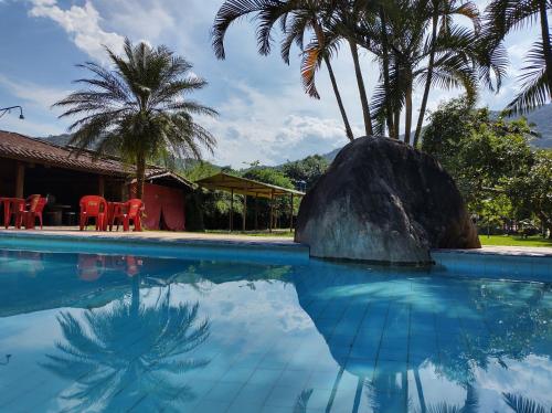 a pool with a rock and palm trees and red chairs at Pousada Rancho Texas Ubatuba in Ubatuba