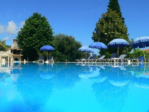 a swimming pool with chairs and blue umbrellas at Apraos Bay Hotel In Kalamaki Beach in Apraos