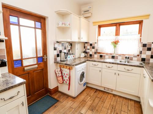 a kitchen with white cabinets and a washer and dryer at Gromit Cottage in Ripon