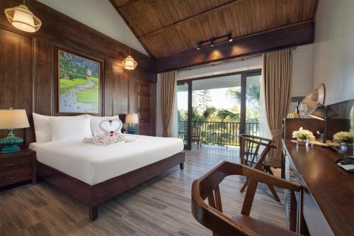 a bedroom with a bed and a desk and a table with a chair at Bai Dinh Riverside Resort & Spa in Ninh Binh
