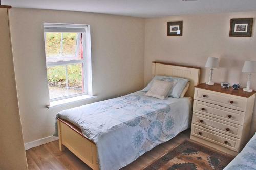 a bedroom with a bed with a dresser and a window at Glenbeigh Holiday Cottage - Tigin Mamo in Glenbeigh