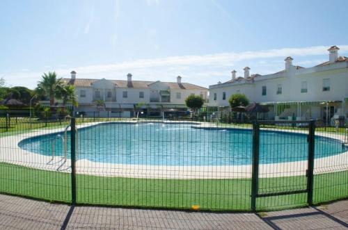 a fence around a swimming pool in front of houses at Casa adosada con porche, piscina y pista de pádel, junto al campo de golf in El Portil
