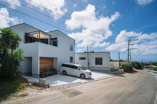 a white car parked in front of a white house at ととのいVilla YAE in Motobu