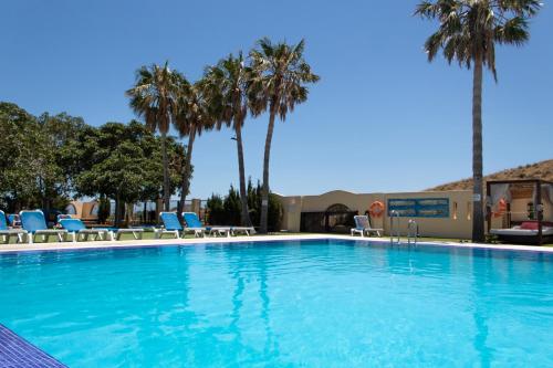 a large swimming pool with blue chairs and palm trees at Kampaoh Los Escullos in Almería