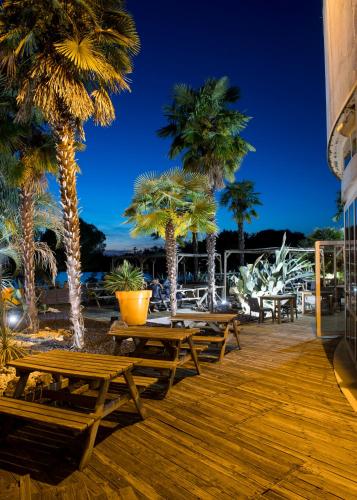 a deck with picnic tables and palm trees at night at L'hôtel by JOA de Saint-Paul-Lès-Dax in Saint-Paul-lès-Dax