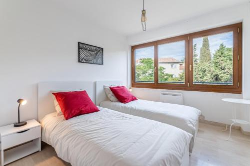 2 Betten mit roten Kissen in einem Zimmer mit Fenster in der Unterkunft Leï Tapenié 2 par Dodo-a-Cassis in Cassis