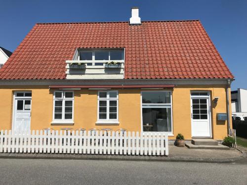 a yellow house with a red roof and a white fence at Havnevej 18, stuen, Ballen in Ballen